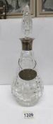 A cut glass decanter with silver collar and white metal label