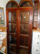A dark wood display cabinet with double bow top