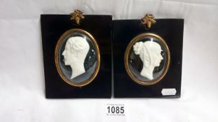 A pair of relief plaster silhouettes under domed glass on ebonised backs with bronze oak leaf