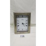 A silver framed clock with silver panel to rear