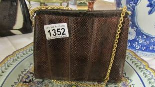 A brown vintage snakeskin handbag with yellow metal shoulder chain
