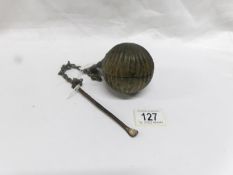 A heavy ball shaped object on chain that opens to reveal a receptacle and with spoon