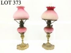 A pair of pink satin glass peg font oil lamps on ormolu brass bases (1 shade chipped)