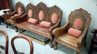 A heavily carved hardwood 3 piece suite with upholstered panels and bolster cushions