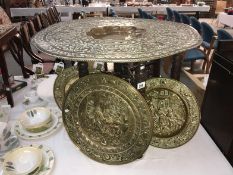 A large Indian brass topped table on folding carved base and 3 brass plaques