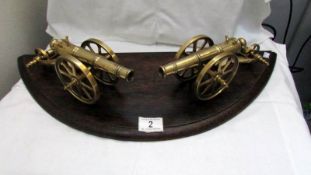 A pair of brass cannons on an oak base