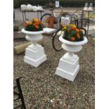 Pair of painted cast iron urns on plinths.