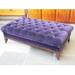 A large purple button velvet pouffee on oak legs. L158cm D90cm H50cm.