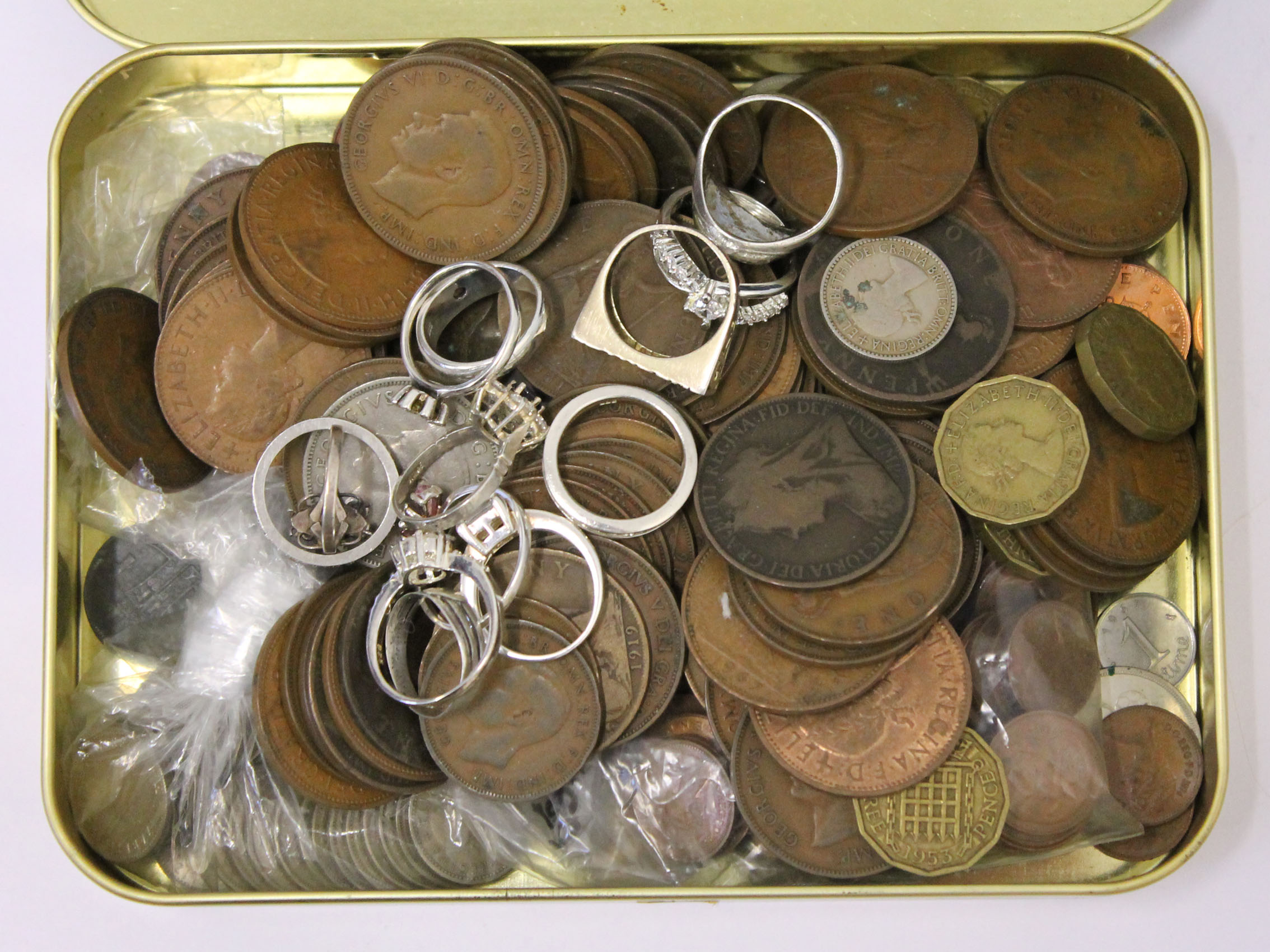 A tin of coins and various silver rings.