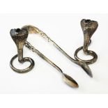 A pair of white metal cobra snakes marked 'KAA' and a pair of hallmarked silver sugar tongs.