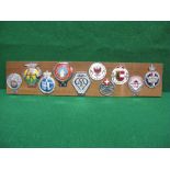 Ten car badges mounted on a wooden board to include early AA,