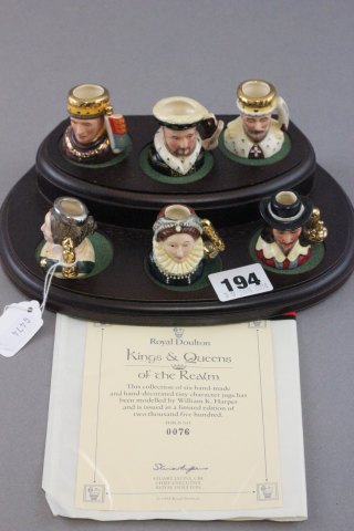 Set of six tiny Royal Doulton Kings & Queens of the realm character jugs on wooden display stand -