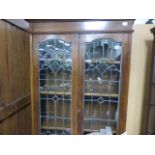 An Art Nouveau oak twin leaded glass display cabinet; raised on a base of two doors