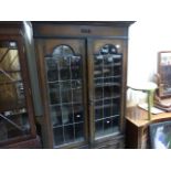 An early 20th century oak twin leaded glass door cabinet; raised on a base of two panelled doors