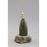 A green hard stone; of conical shape; surmounted with a small gilt pixie