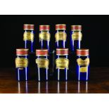 A Set of Eight Cylindrical Blue Glass Chemist's Jars with painted tin lids and gilded scroll labels,