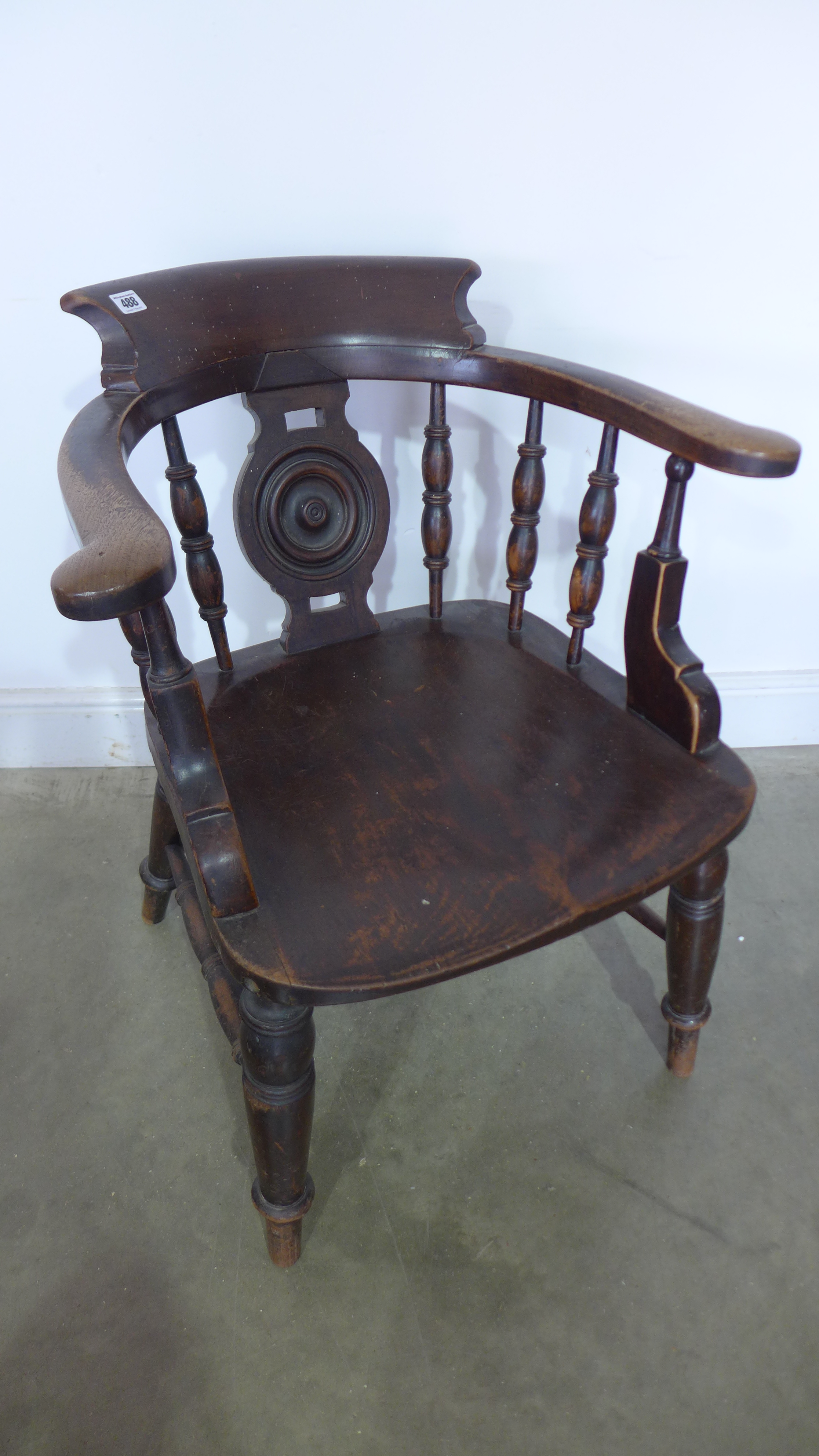 A dark stained elm smokers bow desk chair with a circular centre splat flanked by turned spindles