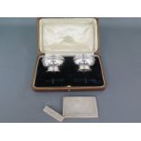 A pair of silver hallmarked salts with blue glass liners and a silver card case with engine turned