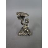 A small silver hallmarked candlestick in the form of a seated child holding a flower - Height 5.