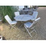 A used folding hardwood garden table with four folding chairs and cushions