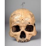 A Borneo skull with incised foliate and scroll decoration one side with a large fracture 15cm high.