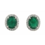 A pair of emerald and diamond cluster ear studs, the oval-shaped emeralds are set within a