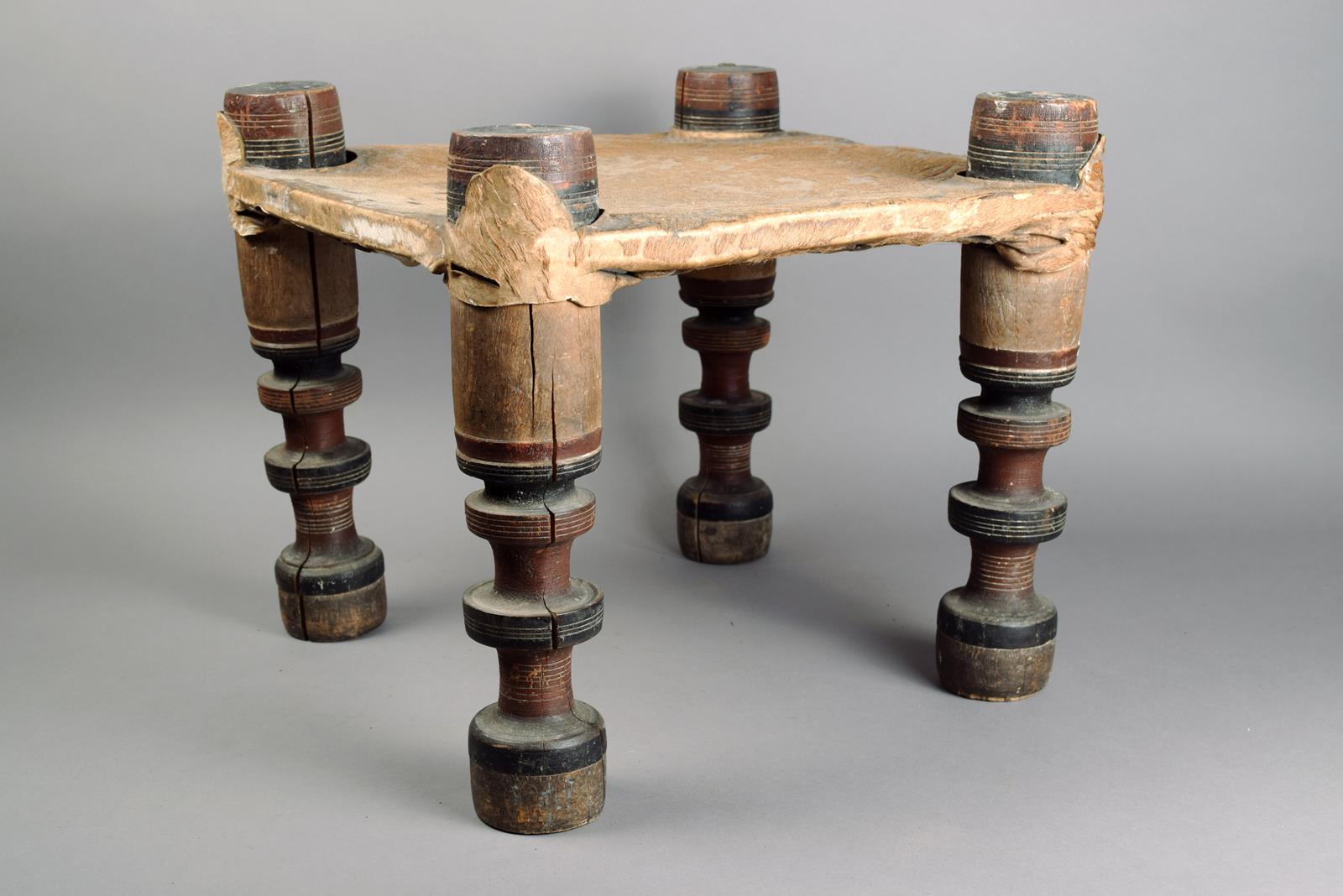 A North African stool wood, with polychromed turned wood legs and with a hide covered seat, 34cm