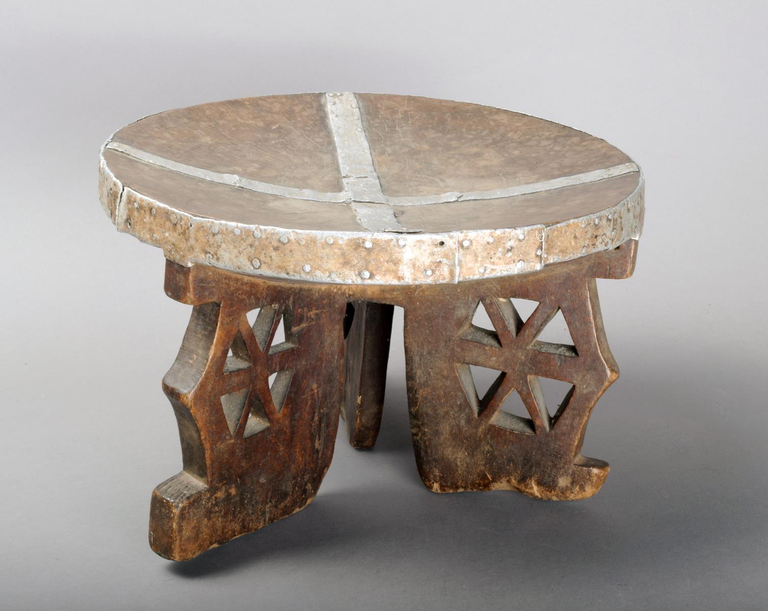 A Kamba stool Kenya wood, with applied aluminium bands and with pierced legs, 18cm high.