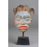 A Haida maskette North West Coast carved wood, with shell eyes and hair tufts, 9.5cm high, on a