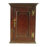 A George II oak hanging wall cupboard, with a fielded panel door enclosing a green painted