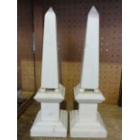 A pair of white marble obelisks mounted on stepped square plinths, each raised on four bun supports,