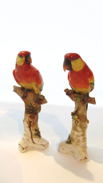 A pair of Samson type models of parrots with red, yellow and green plumage, both perched on branches