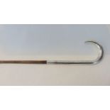 A slender bamboo walking cane terminating in an extensive silver crooked handle with chased detail