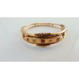 An Edwardian bangle, set with three graduated pink stones, possibly ruby, interspersed with two