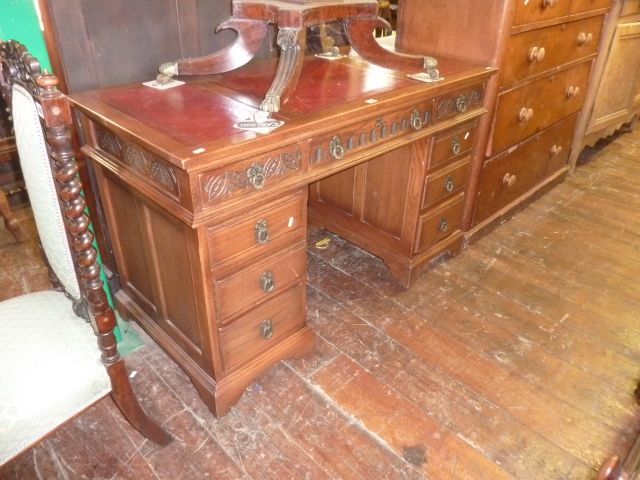 A pedestal oak writing desk of nine drawers with carved detail and inset leather top, 130cm