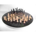 A worked stained hardwood chess set, the board of circular form with incised detail of African