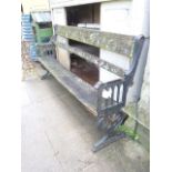 A gothic revival garden bench with weathered timber slatted seat and back raised on a pair of