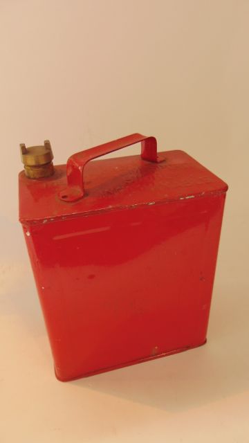 A vintage fuel can with all over red painted finish and impressed text reading Petroleum Spirit