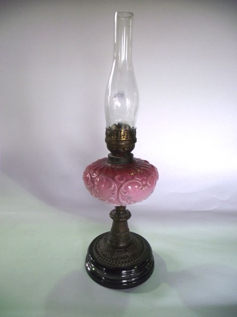 A Victorian oil burning lamp raised on an embossed base accommodating an opaque cranberry shade with