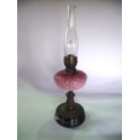 A Victorian oil burning lamp raised on an embossed base accommodating an opaque cranberry shade with