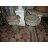 A pair of weathered cast composition stone garden urns with circular squat fluted bowls and combined
