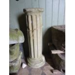 A weathered natural stone pedestal of cylindrical form with fluted column and stepped circular base,