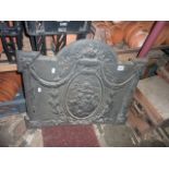 A cast iron fire back with decorative raised relief cherub, flowering urn, trailing swag and further