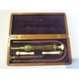 A late 19th/early 20th century cased enema assembly, the brass syringe with turned ivory handle with