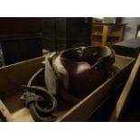 A shallow wooden crate containing a selection of vintage leather horse harness, bits, leather nose