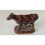 A 19th century model of a standing cow with all over mottled brown glaze and raised on an oval base