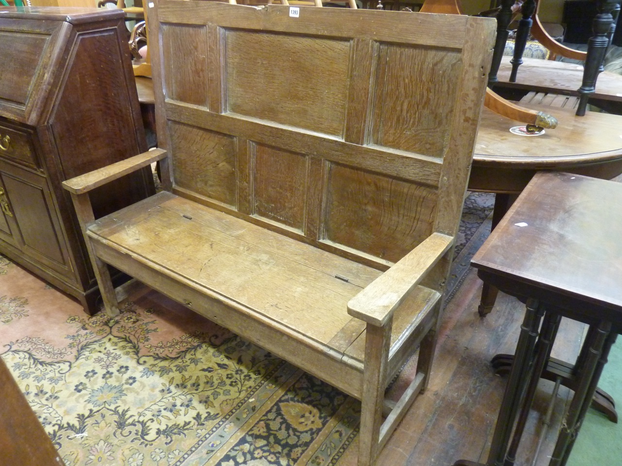 A small Georgian oak settle with panelled back, the shallow box seat with rising lid, raised on