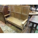 A small Georgian oak settle with panelled back, the shallow box seat with rising lid, raised on