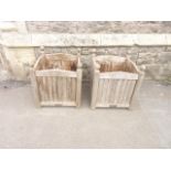 A pair of weathered teak planters of square cut form with turned finials and vertical slatted panels