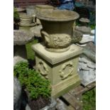 A buff coloured cast composition stone garden urn of circular waisted form with grape and vine